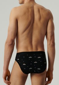 Czarne slipy z płaskim pasem w talii, z powtarzającym się wzorem logo koszykówki. Materiał wydaje się gładki i elastyczny.