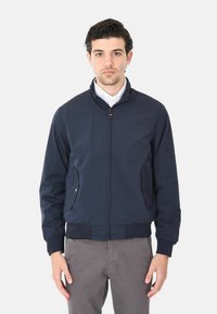 Giacca bomber della marina realizzata in tessuto leggero. Presenta una chiusura con zip, due tasche laterali e polsini e fondo a coste. Design minimalista.