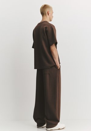 Braunes übergroßes T-Shirt und passende weit geschnittene Hosen aus weichem Stoff mit einer Taschendetailierung, kombiniert mit weißen Sneakers.