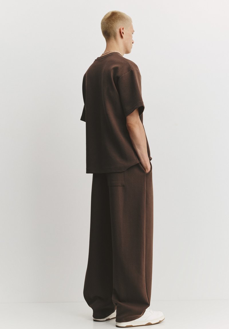 Brązowy oversize t-shirt i pasujące szerokie spodnie, wykonane z miękkiego materiału, z detalem w postaci kieszeni, zestawione z białymi sneakersami.
