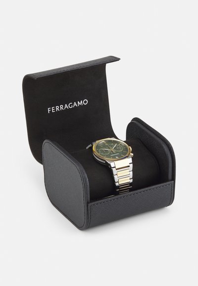 Ferragamo watch in a black display box. Watch features a green dial, gold accents, and a two-tone metal bracelet. Box has a soft interior.