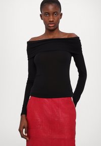 Zwart off-the-shoulder top met lange mouwen, gemaakt van rekbaar materiaal, gecombineerd met een textuurachtige rode leren rok met zijritsen.