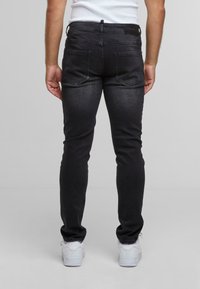 Tamno sivi uski traperice od denima, s dvije stražnje džepove standardnog dizajna i minimalističkim hardverom, uparene s bijelim tenisicama.