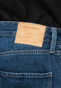 Ceinture de jeans en denim avec une étiquette en cuir fauve cousue indiquant « JACK & JONES Jeans Intelligence Since 1990 Craftsmanship and Dedication. »