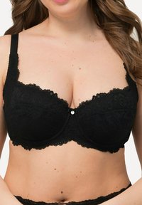 Sostenitore in pizzo nero con ferretto, caratterizzato da motivi floreali, bordi scallop e un fiocco decorativo al centro, con spalline regolabili.