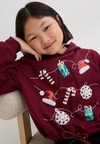 Felpa bordeaux con design di paillettes raffiguranti bastoncini di zucchero, fiocchi di neve, regali e cappelli di Babbo Natale appesi a una stringa decorativa. Tessuto morbido, vestibilità comoda.