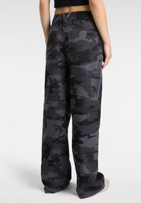 Camo print wide-leg pants in shades of gray and black, featuring back pockets and a checkerboard waistband detail.
