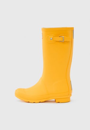Botte de pluie en caoutchouc jaune avec un bout rond, une surface texturée, une sangle réglable avec boucle, et un petit talon pour la stabilité.