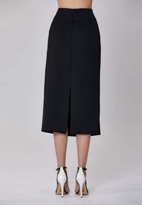 Jupe midi noire avec une fente arrière, design structuré et texture lisse. Associée à des chaussures à talons blancs avec des accents noirs.