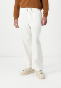 Hvite, løstsittende bukser med elastisk liv og snøring, laget av teksturert stoff, kombinert med offwhite sneakers.