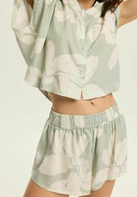 Koszula z krótkim rękawem w kwiatowy wzór i dopasowane szorty w jasnym zielonym i białym kolorze. Lekka tkanina, luźny krój, z elastycznym pasem.