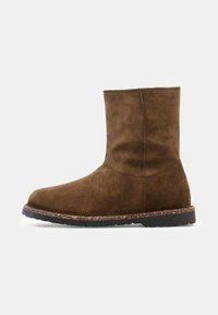 Bruine suède enkelboot met een ronde neus, minimale naden en een gestructureerde rubberen zool. Strak ontwerp, schacht van gemiddelde hoogte.