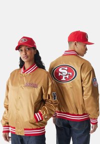 Giacca da baseball in satin dorato con polsini a righe rosse e bianche, con ricamo "49ERS" e logo NFL sulla manica, mostrata frontalmente e posteriormente.