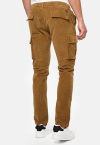 Braune Corduroy-Cargo-Hosen mit Seitentaschen, elastischem Bund und schmal zulaufendem Bein, kombiniert mit weißen Sportschuhen.