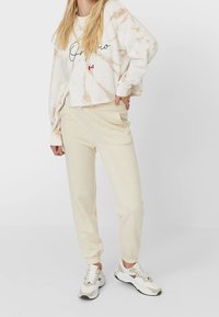 Crème tie-dye sweatshirt met een cropped ontwerp en zwarte scripttekst. Gecombineerd met beige joggers met elastische boorden en zijzakken.