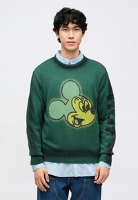 Zöld kötött pulóver nagy sárga és fekete Mickey egér grafikával az elején, és fekete "HUF" felirattal a ujján.