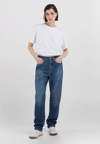 T-shirt bianco a maniche corte abbinato a jeans blu dal taglio ampio. I jeans hanno una lavatura sbiadita e dettagli di cucitura sottili. Indossati con sneakers bianche.