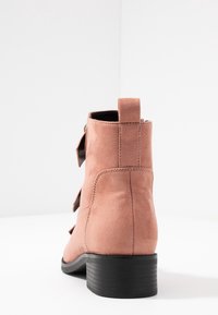 Semišové kotníkové boty v jemné růžové barvě s černým texturovaným podpatkem, s poutkem na zadní straně a prošíváním podél švů.