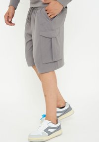 Grå cargoshorts i mjukt material, med framfickor och en sidoficka, i kombination med vita och grå sneakers.