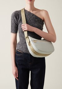 Gray textured sweater with one short sleeve paired with dark denim. Light gray shoulder bag with gold accents and a patterned strap.