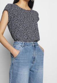 Top nero con motivi floreali e maniche arrotolate, abbinato a jeans alta vita di colore azzurro chiaro. Presenta delicati motivi floreali e tasche frontali.