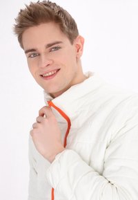 Jachetă albă matlasată cu detalii închise cu fermoar portocalie. Gulerul este înalt, iar materialul pare moale și neted. Prezintă un design simplu.