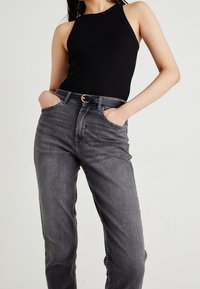 Svart ribbad linne i kombination med högmidjade grå denimjeans, med ett synligt svart bälte med guldspänne och fickor.