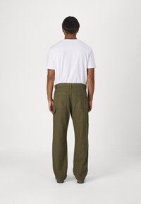 Green cargo pants with a relaxed fit, featuring side pockets, stitched details, and a waistband. Paired with a simple white t-shirt.