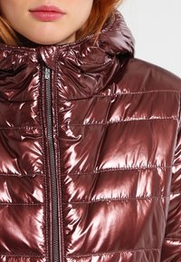 Metallic burgundy puffer jacket with a zipper closure and hood. Features quilted sections and a glossy texture.