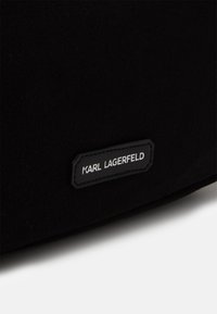 Černá tkanina s malou obdélníkovou černou nášivkou, na které je bílý text "KARL LAGERFELD".