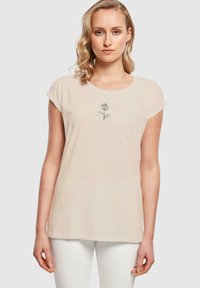 Lys beige t-skjorte med korte ermer og rund halsringning, med et svart linjeteiknede rose-design på midten foran. Glatt bomullsstoff.