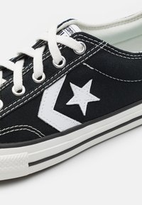 Svart lerret sneakers med hvit stjerne og chevron-design, runde snører og kontraststing. Har gummisåle og tåhette.