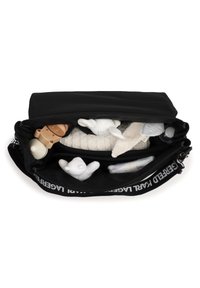 Geantă neagră cu partea superioară prevăzută cu fermoar, plină cu jucării pentru copii și o pătură albă tricotată cu textură vizibilă în interior. Breteaua are un text în contrast.