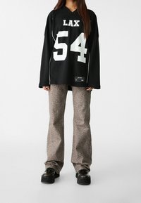 Maillot noir à manches longues avec le texte blanc « LAX » et le numéro « 54 », accompagné d'un pantalon évasé imprimé léopard marron et de chaussures plateformes noires.