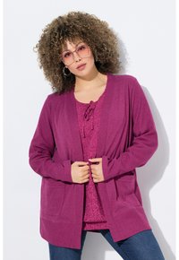 Lila Strickjacke aus weichem Strickstoff, mit langen Ärmeln, offener Vorderseite und zwei vorderen Taschen, übereinander getragen mit einem passenden Oberteil.