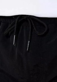 Shorts noirs en tissu doux, avec une taille élastique à cordon de serrage et des embouts en métal. Pas de motifs ni de logos visibles.