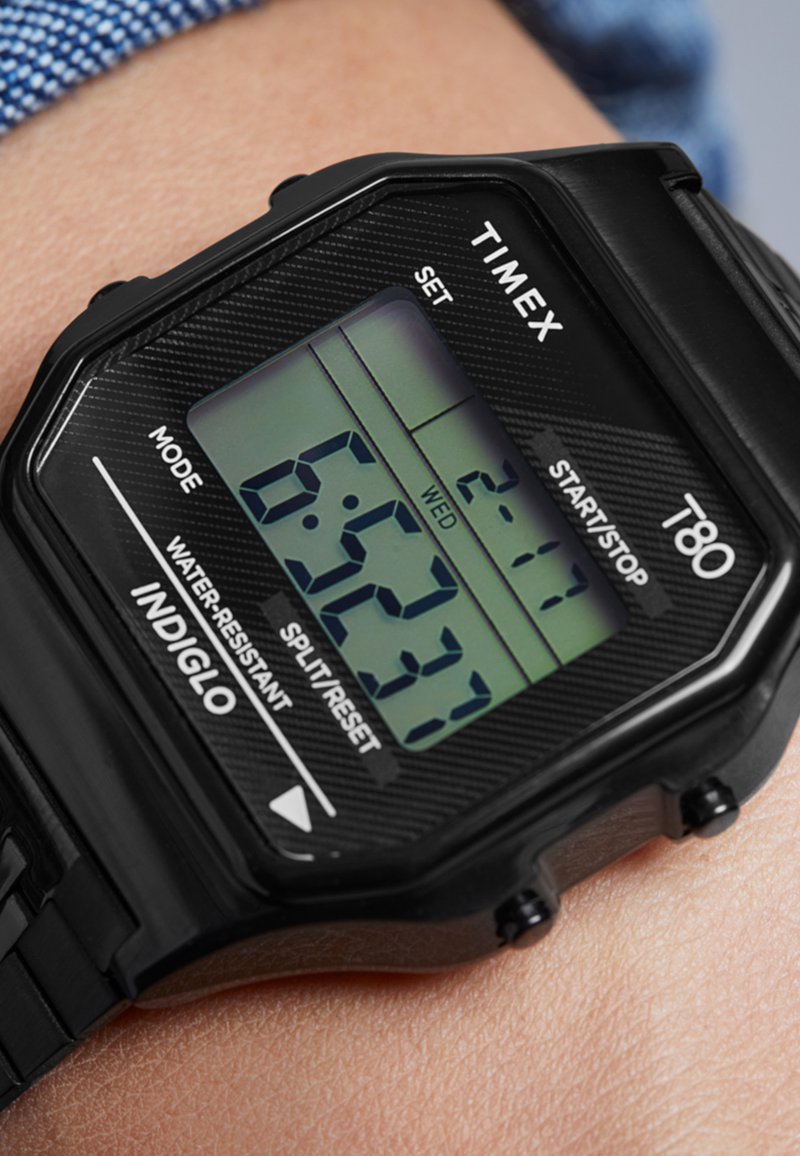 Orologio digitale nero con cassa esagonale, dotato di display retroilluminato verde, controlli etichettati per modalità, impostazione e avvio/arresto, indossato a un polso.