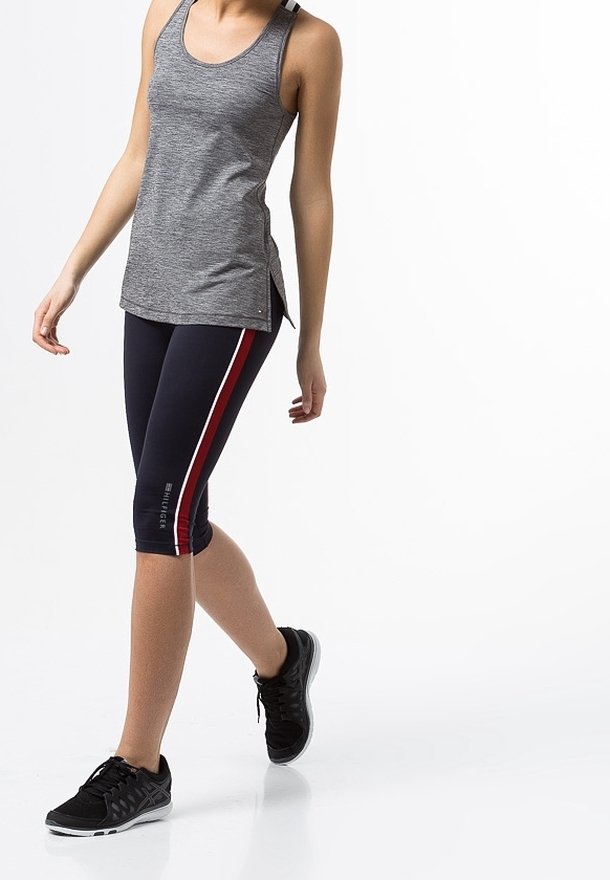 Grijze sporttanktop met een ontspannen pasvorm, gecombineerd met marineblauwe capri-legging met rode zijstrepen. Zwarte hardloopschoenen maken de outfit compleet.