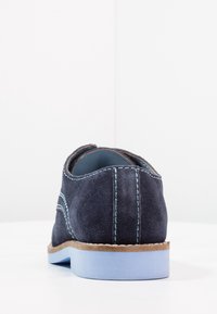 Scarpa in suede blu marino con suola azzurro chiaro, caratterizzata da cuciture a contrasto e forma arrotondata. La vista posteriore mette in evidenza la texture liscia e il minimo hardware.