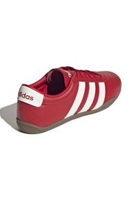 Röda lädersneakers med tre vita ränder, klassisk design, rund tå och texturerad gummisula med fiskbensmönster.