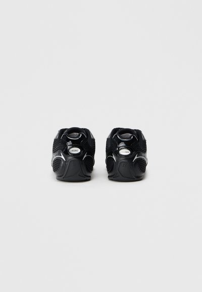 Par de zapatillas negras de Marc Jacobs mostradas desde atrás sobre un fondo blanco liso, destacando los logotipos de la marca y los detalles texturizados.