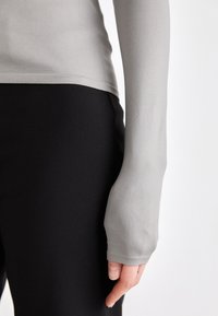 Light gray long-sleeve top with fitted design, smooth texture, and thumbhole detail paired with black leggings, showcasing a seamless look.