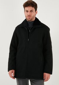 Giacca nera con un tessuto morbido e texturizzato, chiusura con zip e colletto alto. Presenta tasche laterali e un design dal fit rilassato.