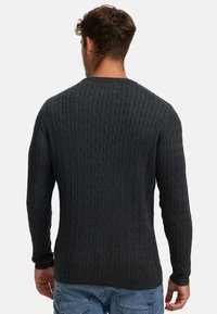Mørkegrå kabelstrikket genser med lange ermer, rund hals og teksturerte mønstre, kombinert med blå jeans.