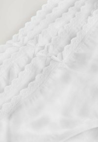 Weiße Baumwollunterwäsche mit zarten Spitze-Details und kleinen Schleifen, die eine glatte Textur und gewellte Kanten zeigt.