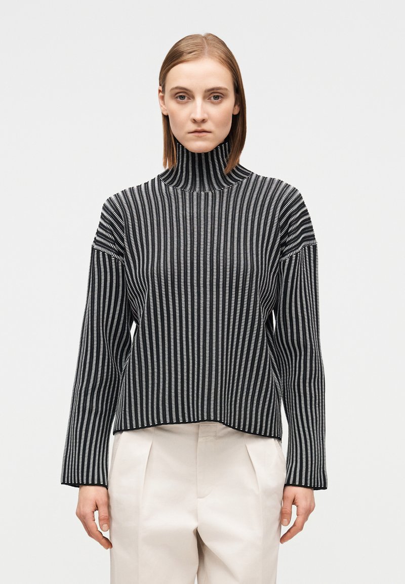 Ριγέ μαύρη και λευκή ζιβάγκο μπλούζα με μακριά μανίκια, υφή με ριμπ και άνετη εφαρμογή. Η γραμμή του τελειώματος είναι ίσια και ομοιόμορφη.