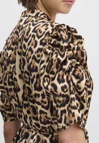 Leopardenmusterkleid mit puffigen Ärmeln, das ein satinartiges Finish aufweist. Die Farben umfassen Beige, Schwarz und Braun und betonen kräftige Tiermuster.