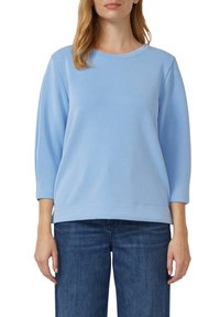 Jasnoniebieska bluza z okrągłym dekoltem, rękawami do łokcia i luźnym krojem, wykonana z miękkiego, gładkiego materiału.