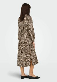 Leopardmönstrad långklänning med långa ärmar, midjevart, och sidoklipp, i kombination med svarta platta skor. Tillverkad av ett lätt tyg.