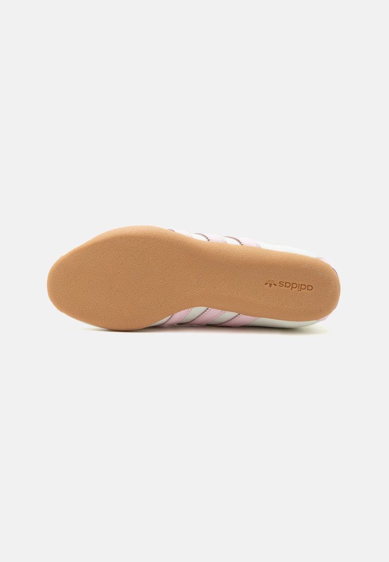 Zool van schoen met lichtbruine, gestructureerde rubberen onderkant en zichtbaar Adidas-logo, met zijkanten van witte en roze bovenstukken.